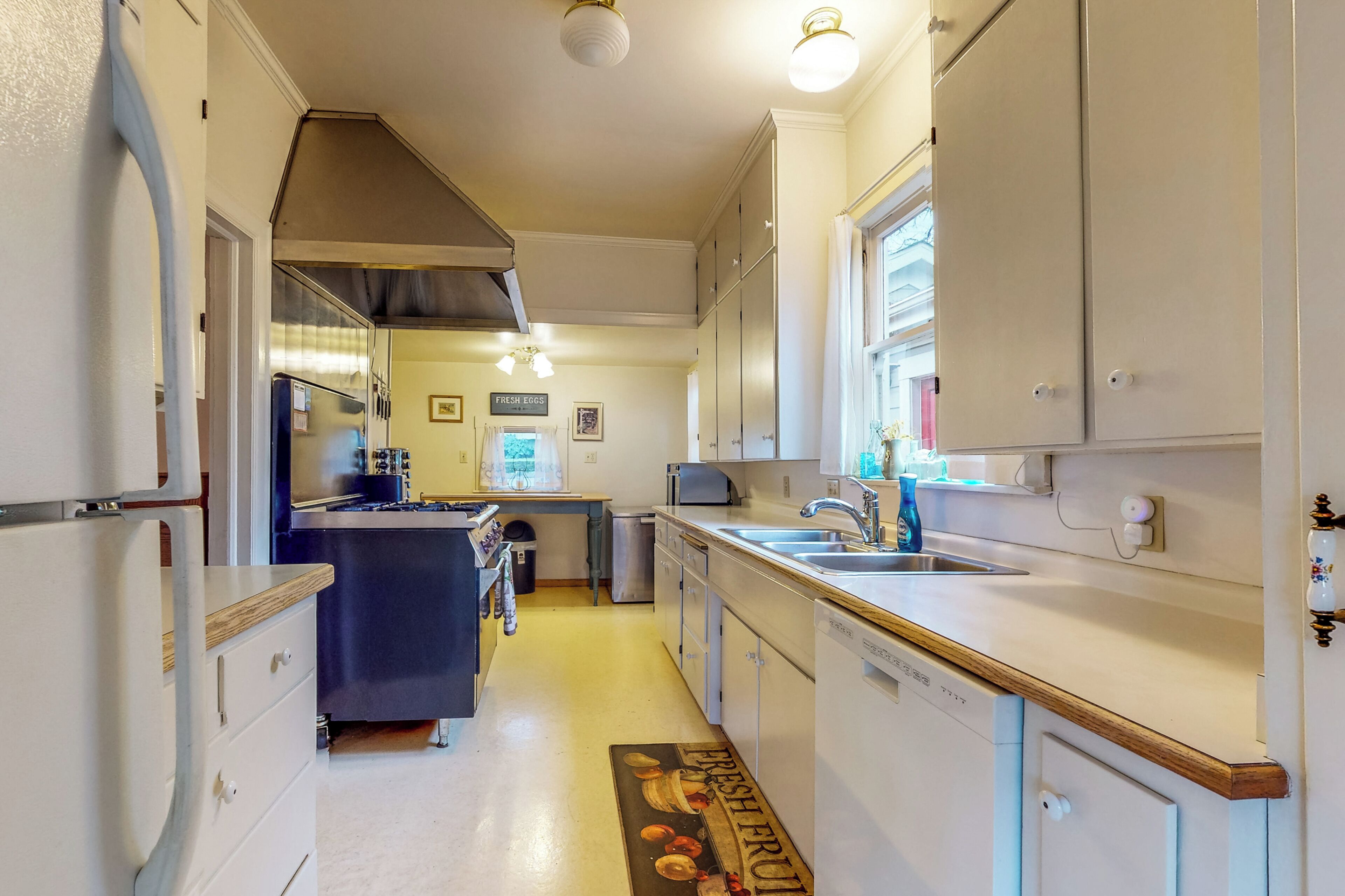A narrow kitchen with white cabinets, a refrigerator, a sink, and a window.