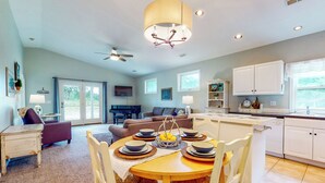 A dining area with a round table, white chairs, and a chandelier. There is a kitchen area with white cabinets and a window. - Homestead Cottage < 2 Mi to Salt Creek (Dallas)