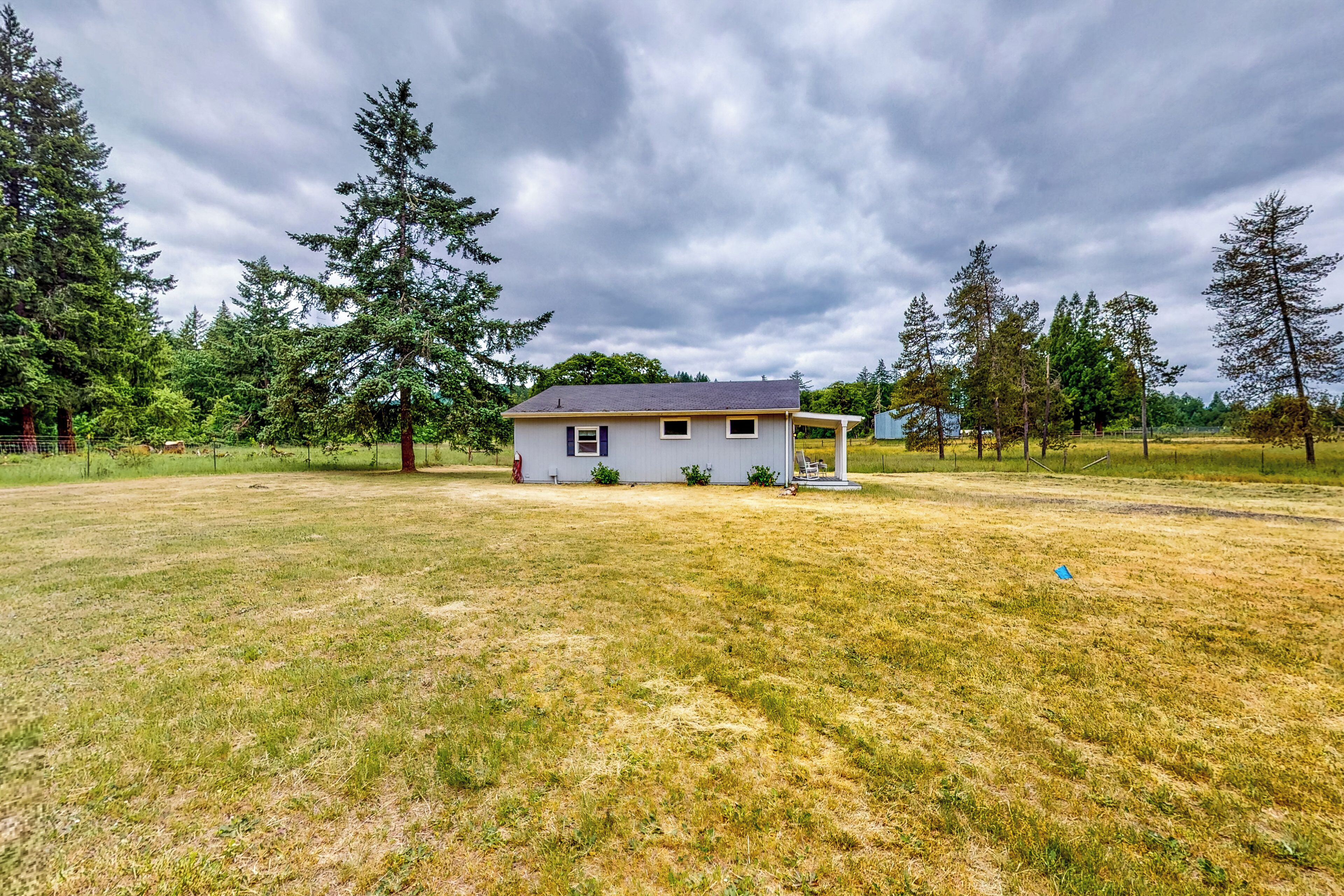 A single-story house with a small porch, surrounded by a grassy field and tall trees.
