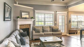 A living room with a fireplace, a ceiling fan, and a large window.