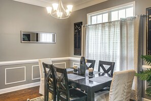 A dining area with a table, chairs, a chandelier, and a window with curtains. - 3 BR Cozy Family Home w/ Playground (Valdosta)