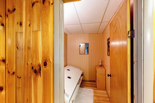 A wooden-paneled room with a bed, a small window, and a door leading to another room. - Sauna! Northern Maine Base Near Snowmobile Trails (Madawaska)