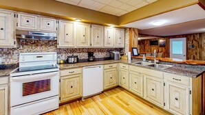 Una cucina con mobili bianchi, piano cottura in acciaio inox, lavastoviglie e schienale piastrellato.