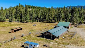 Un ranch comprenant une grande grange, une remorque et un espace clôturé où se trouve un tracteur.