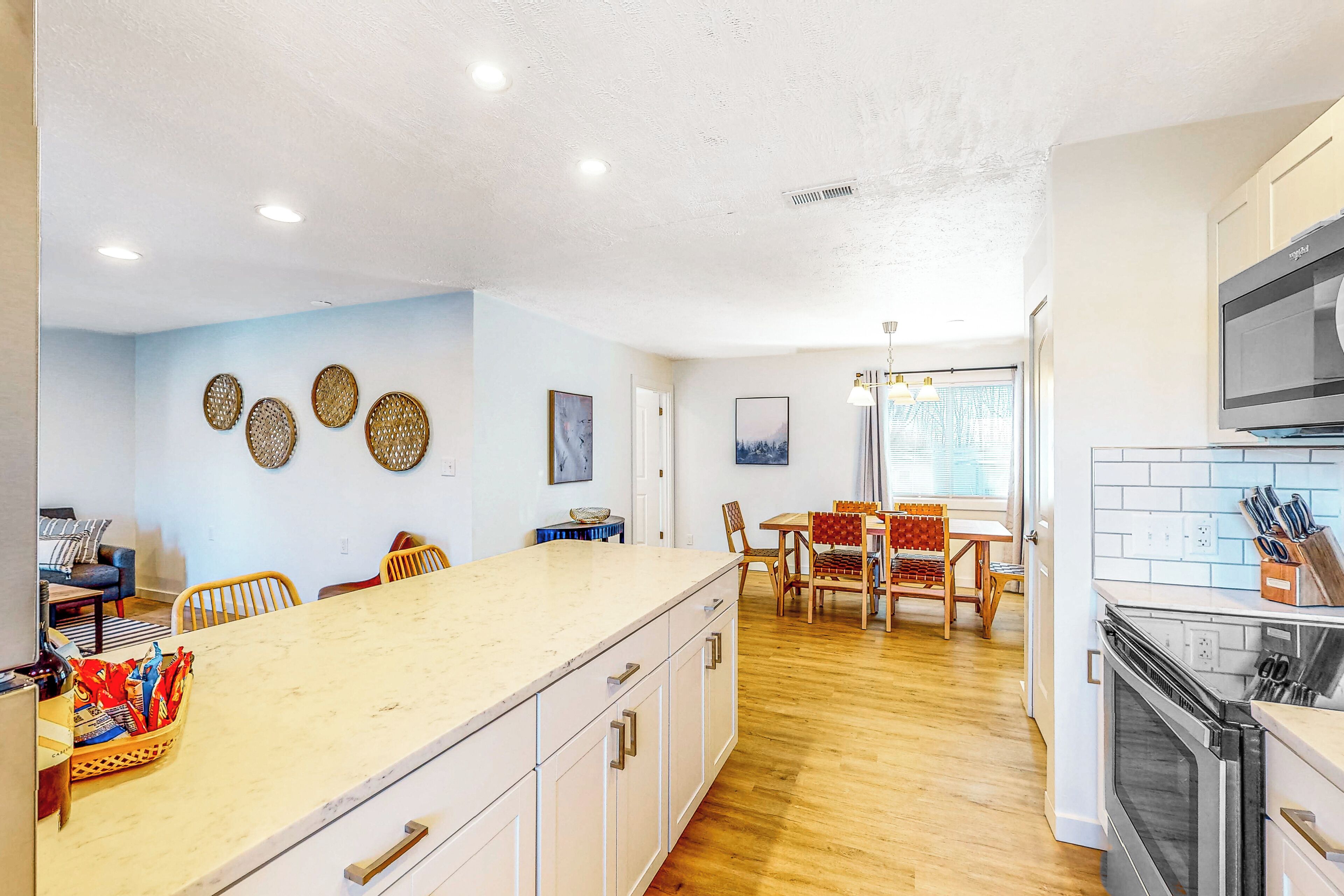 A modern kitchen with a large island, wooden flooring, and a dining area with a table and chairs.