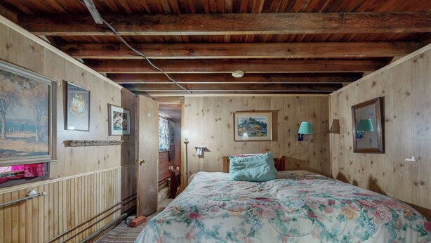 A bedroom with wooden walls, a bed with a floral bedspread, a wooden headboard, and a wooden floor. - 6BR Lakefront Estate w/ Private Piers & Patios (Ripon)