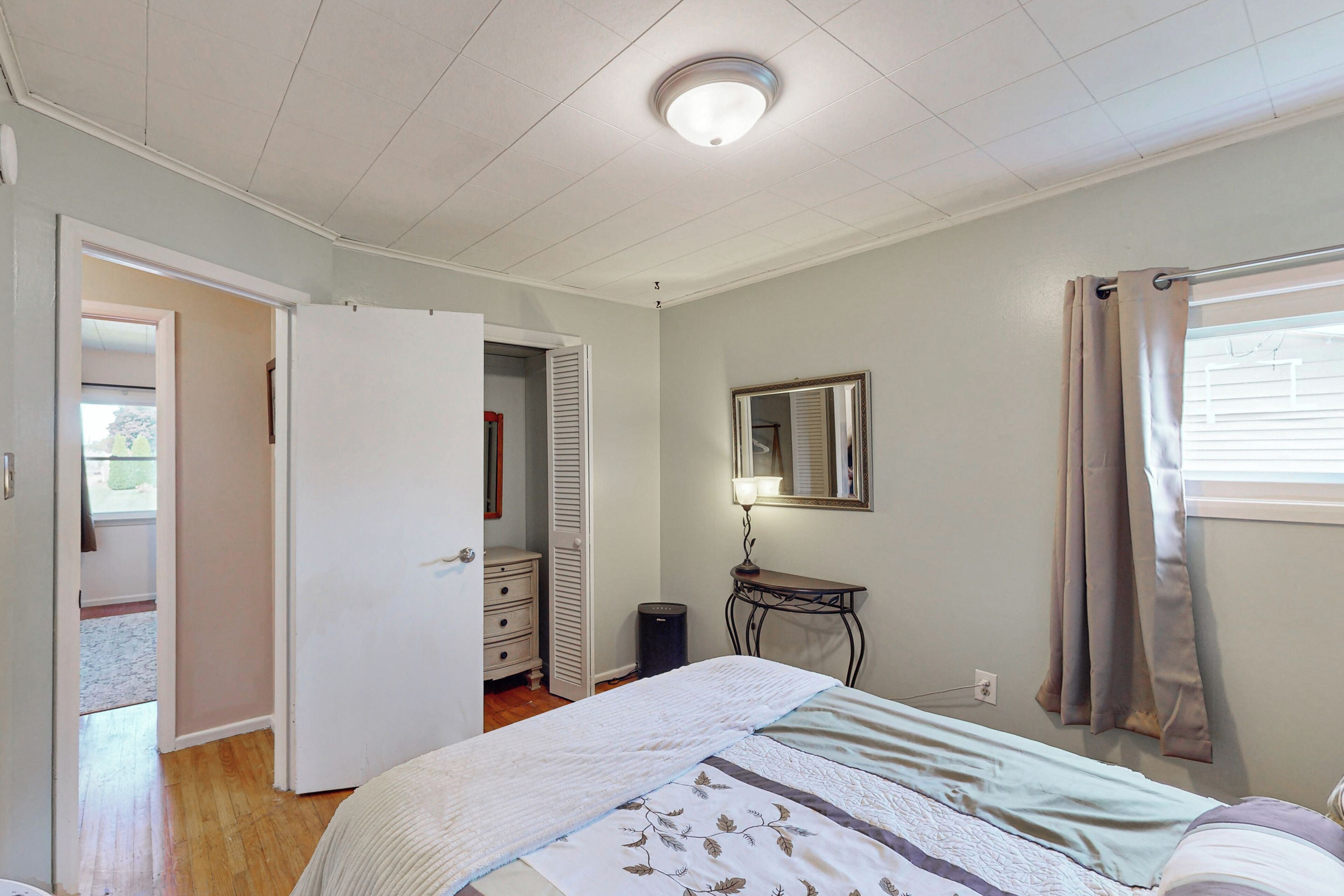 A bedroom with a bed, a dresser, a mirror, and a window with curtains.