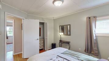 A bedroom with a bed, a dresser, a mirror, and a window with curtains.