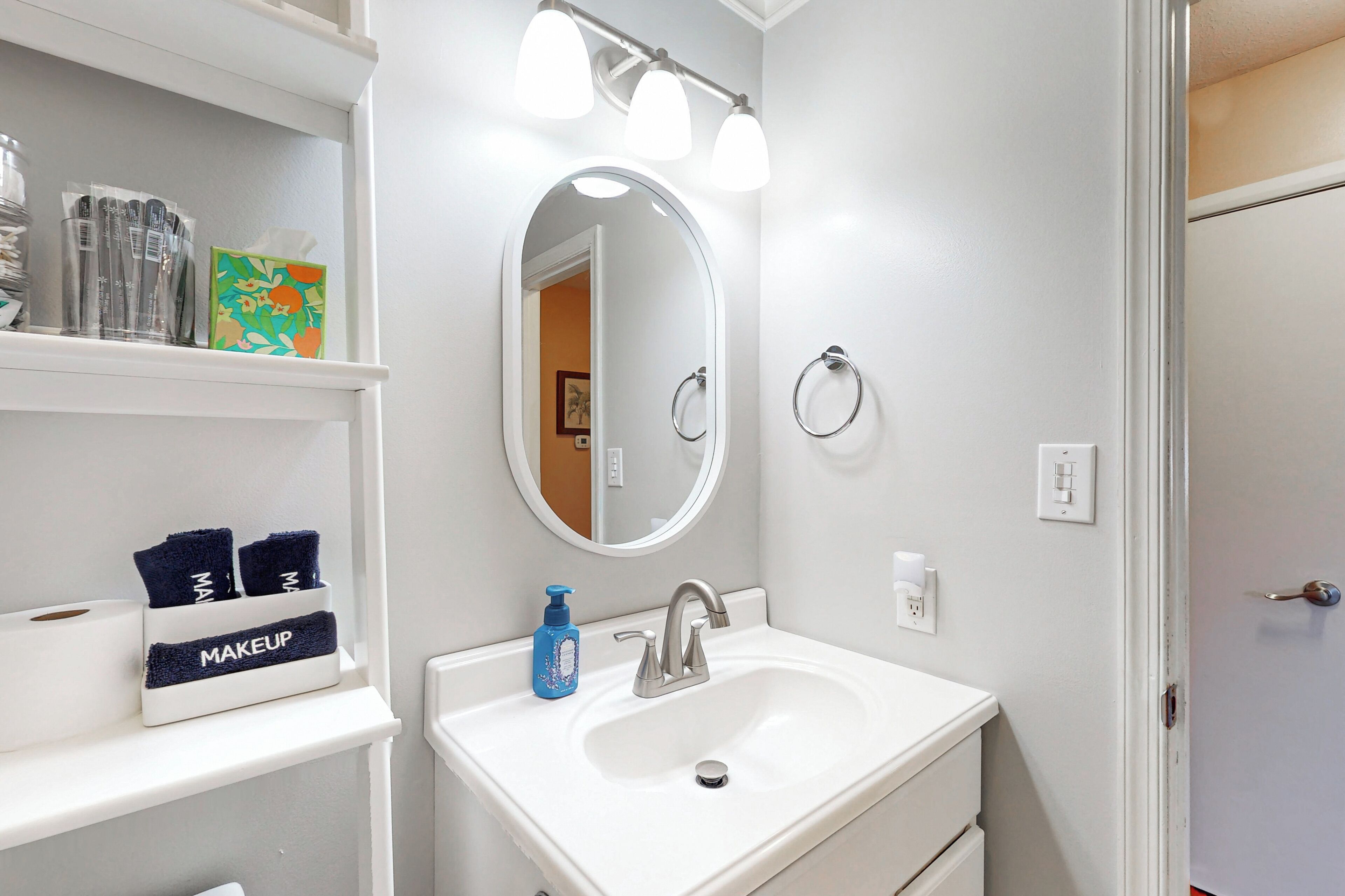 A bathroom with a white sink, a mirror, and a shelf with toiletries.