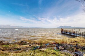 A rocky shoreline with a pier extending into calm waters, surrounded by mountains in the distance. - Forbestown Carriage House in the Heart of Dtwn (Lakeport)