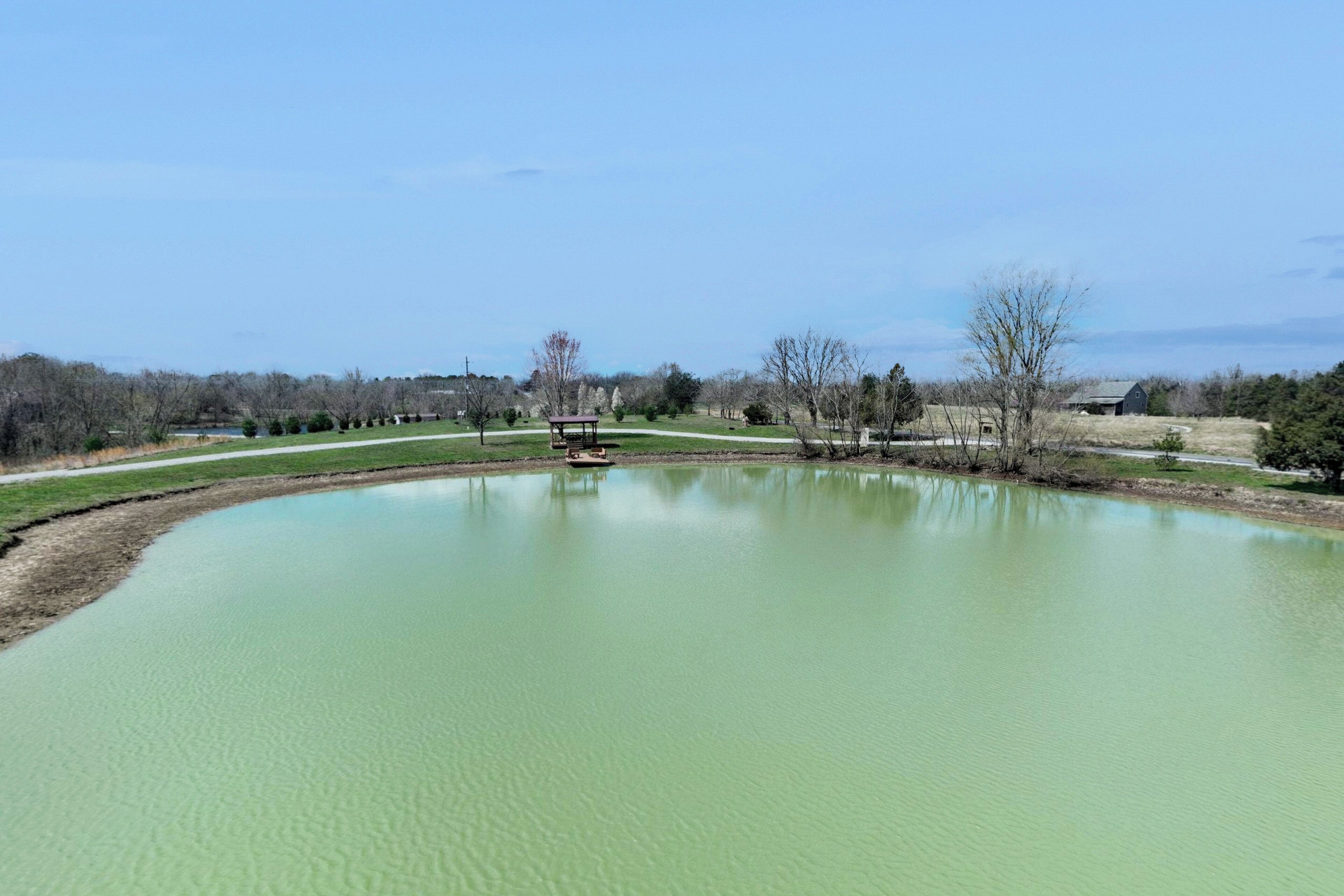 A large, calm pond with a gazebo in the center, surrounded by open fields and sparse trees.