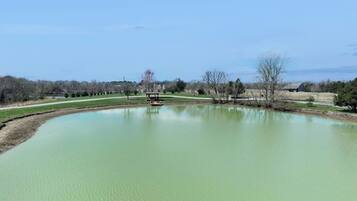 A large, calm pond with a gazebo in the center, surrounded by open fields and sparse trees.