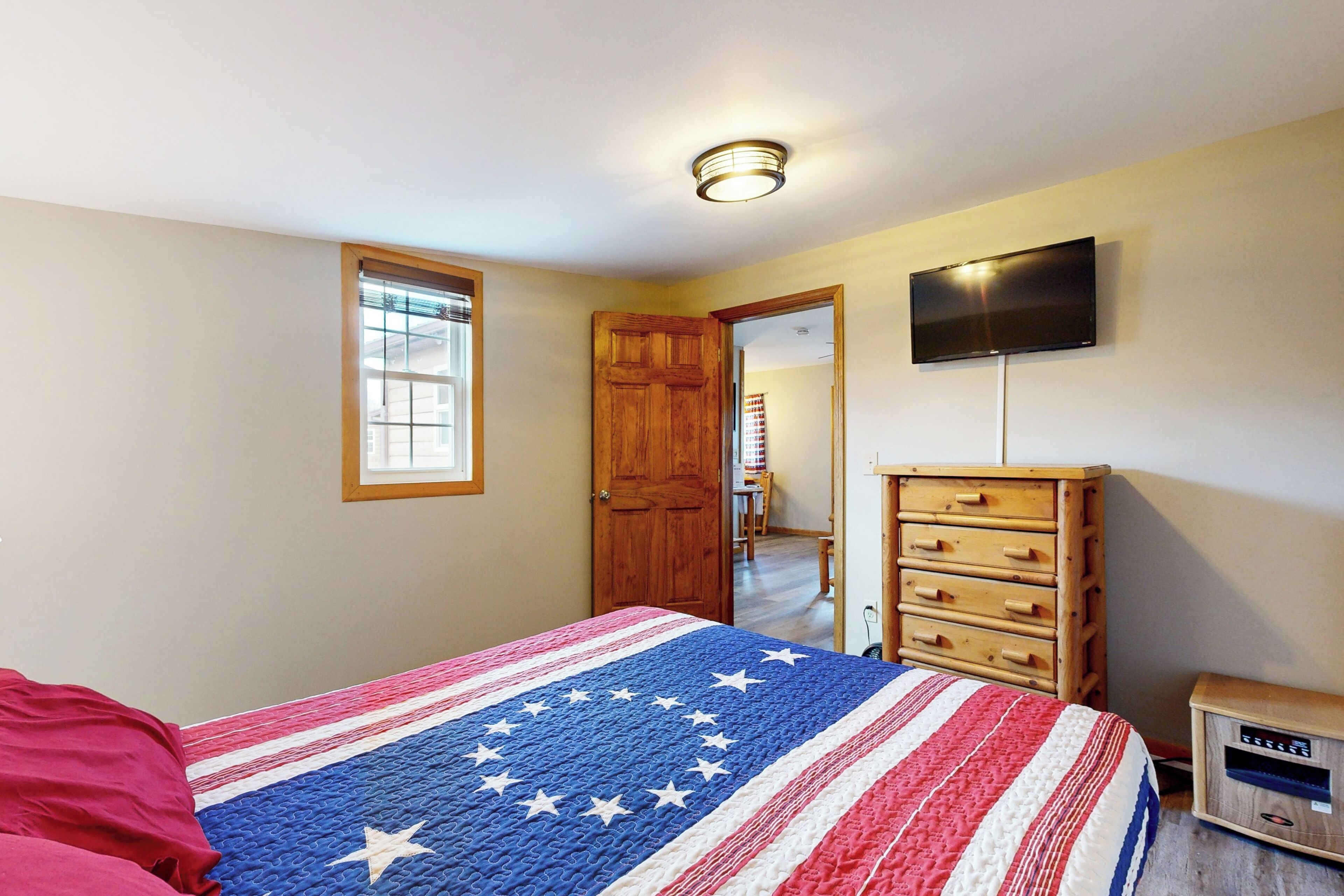 A bedroom with a bed, a wooden dresser, a television, and a window.