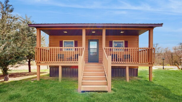 A wooden cabin with a front porch, a staircase, and a door.