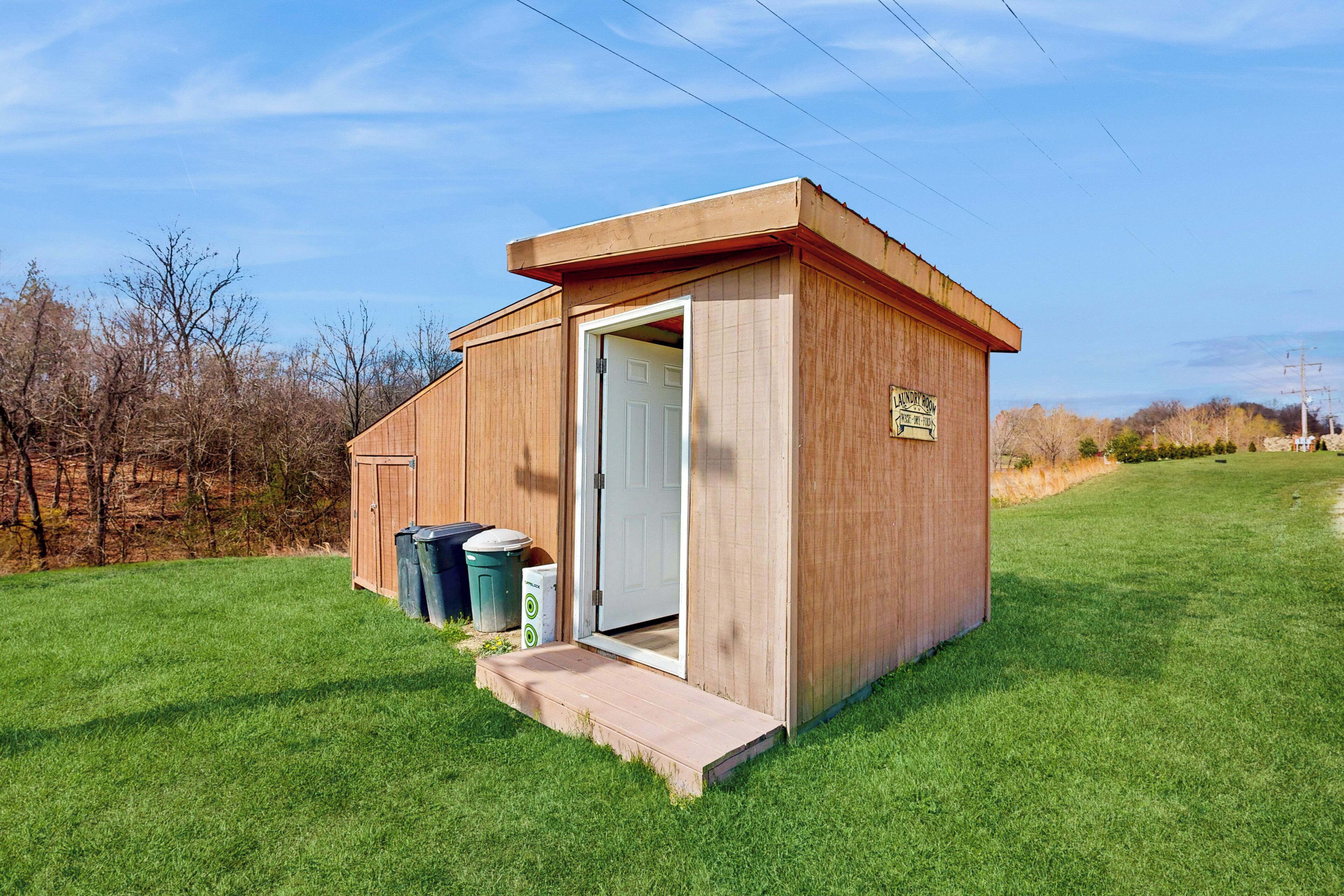 A small wooden structure with a door, a ramp, and two trash bins.