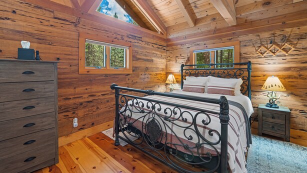 Une chambre dans une cabane en bois, avec un lit, une commode, des tables de chevet et des fenêtres.