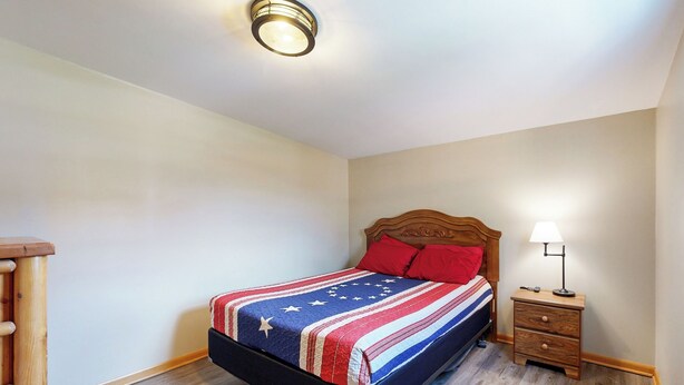 A bedroom with a bed, a nightstand, a lamp, and a wooden dresser. - Blue Line Resort - All 3 Cabins! (Murphysboro)