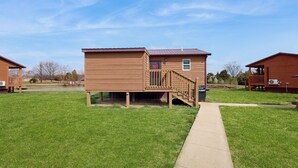 A wooden cabin with a deck, surrounded by a grassy area and a clear sky. - Blue Line Resort - All 3 Cabins! (Murphysboro)