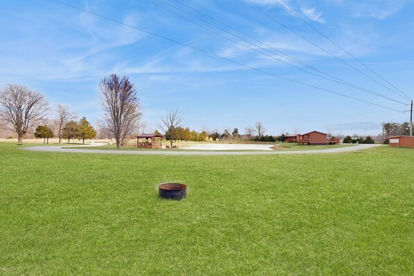 A grassy field with a metal bowl in the foreground, surrounded by trees and buildings in the background. - Blue Line Resort - All 3 Cabins! (Murphysboro)