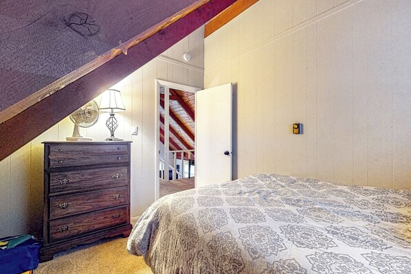 Une chambre à coucher comprenant un lit, une commode et une porte donnant sur un escalier.