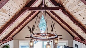Ein rustikales Interieur mit Holzbalkendecke, einer großen, runden, hölzernen Windrad-Leuchtreiter und einem an der Wand befestigten Fernseher.