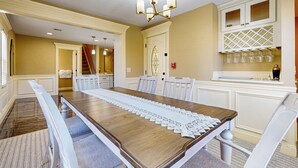 A dining room with a wooden table, white chairs, a lace table runner, a chandelier, and a wine rack with glasses. - Steps to Holyoke Medical Center! Remote-work Hub (Holyoke)