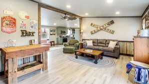 A cozy living room with a rustic wooden coffee table, a leather sofa, and a dining table. A kitchen is visible in the background, and a sign on the wall reads "RAILROAD CROSSING ROAD." - Newly Updated Countryside Home in South Gorin! (South Gorin)