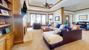 A spacious living room with a large sectional sofa, a wooden bookshelf, and a ceiling fan. - Lakefront Estate: Stunning Views, Deck, Bar & Dock (Bridgeport)