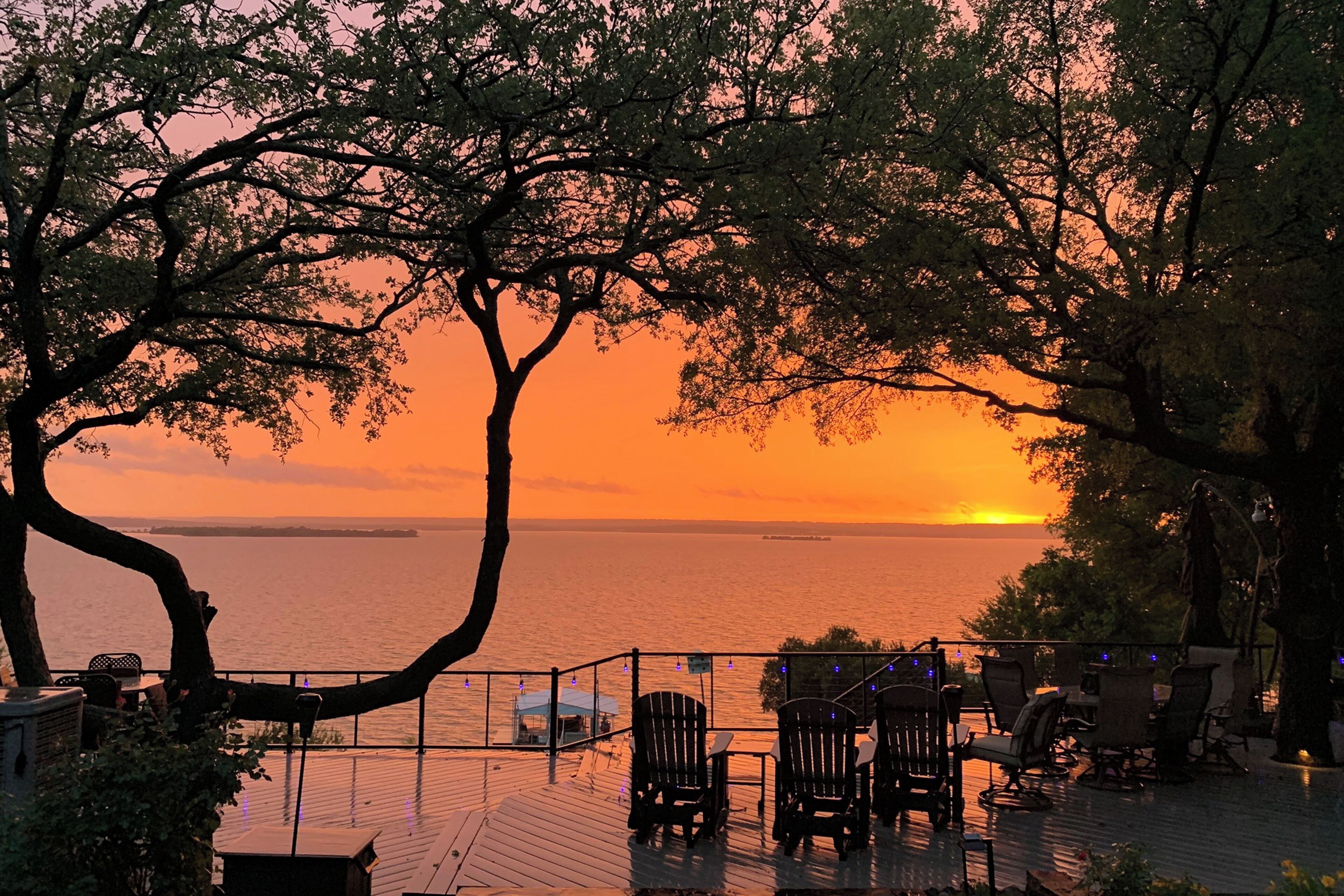 A sunset view from a deck with chairs and tables, overlooking a body of water.