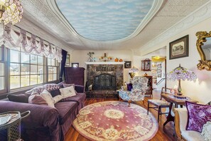 Um quarto com lareira, sofá, poltrona e uma mesa com abajur.