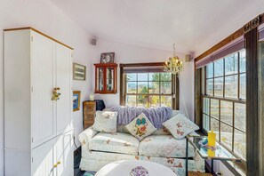 A cozy room with a large window, a sofa with butterfly-themed cushions, and a wooden cabinet.