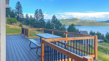 A deck with a table and chairs, overlooking a lake and forested hills.