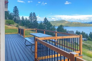 Eine Terrasse mit Tisch und Stühlen, mit Blick auf einen See und bewaldete Hügel.