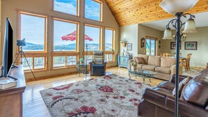 A spacious living room with large windows, a wooden ceiling, and a cozy seating area. - Breathtaking Mountain & Lake Views! (Dayton)