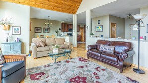 A spacious living room with a wooden ceiling, a beige sofa, a brown leather sofa, a coffee table, and a large rug. - Breathtaking Mountain & Lake Views! (Dayton)
