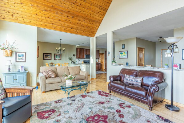 A spacious living room with a wooden ceiling, a beige sofa, a brown leather sofa, a coffee table, and a large rug. - Breathtaking Mountain & Lake Views! (Dayton)