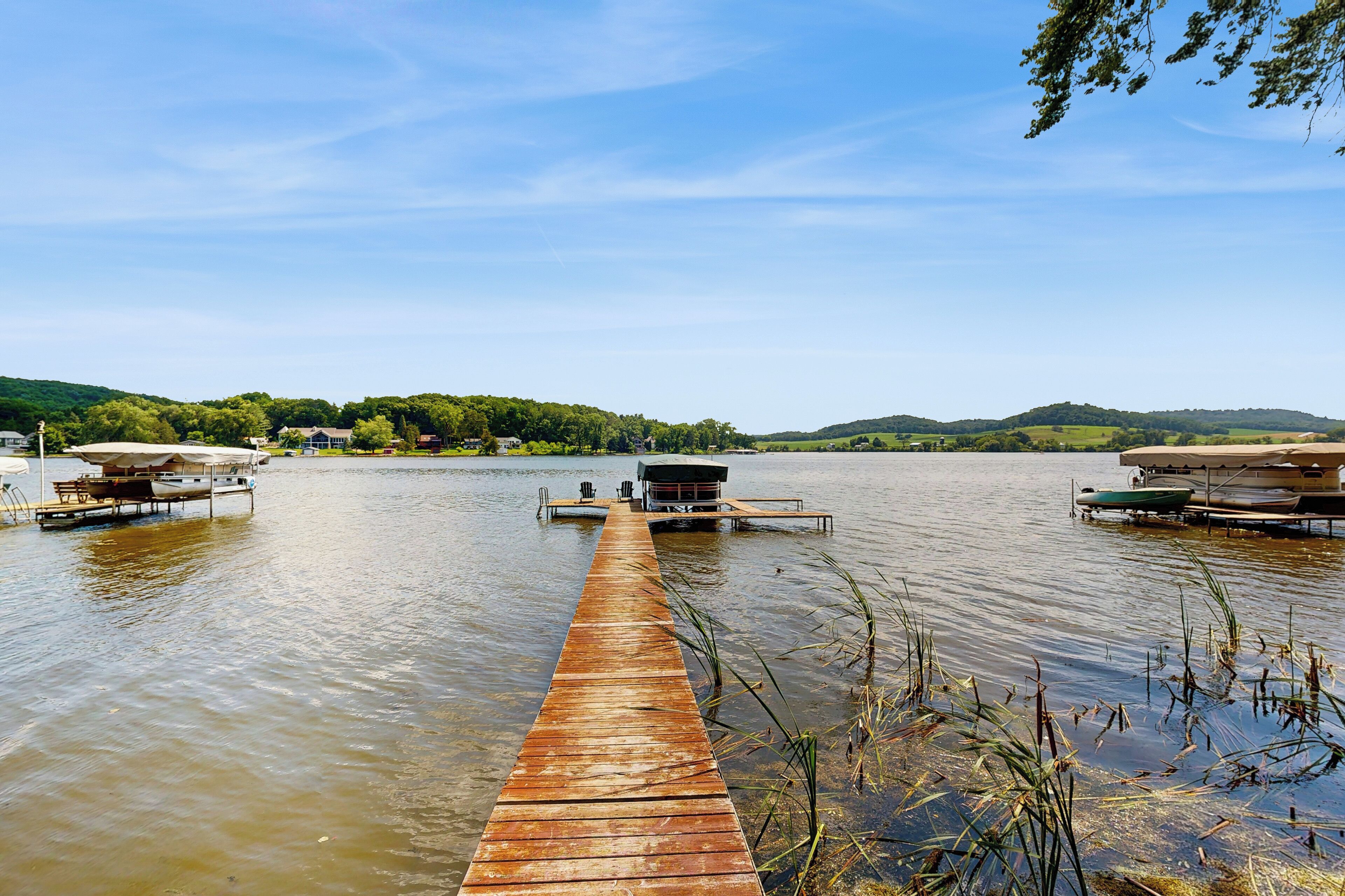 A wooden pier extending into a calm lake with boats docked on either side.