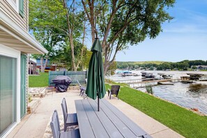 A patio with a table and chairs, a covered umbrella, and a view of a lake with boats.
