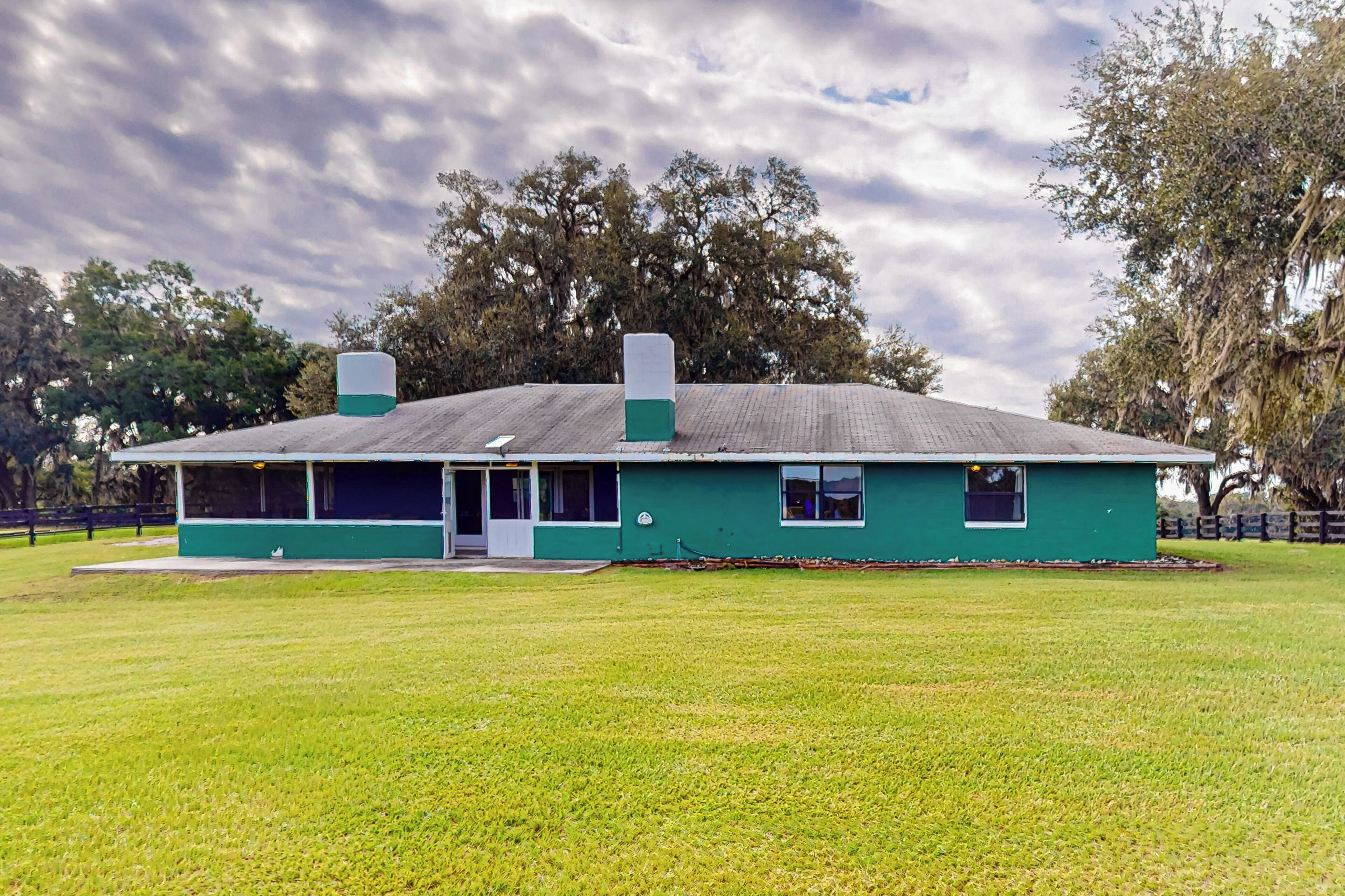 A green building with a flat roof, a front porch, and two chimneys.