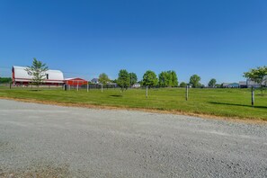 Un paysage rural avec un chemin de gravier, un champ clôturé, une grange rouge et une remorque blanche.