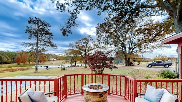 A covered outdoor deck with a stone fire pit, red railings, and two cushioned chairs. - 4BR Waterview Home w/ Pool, Fire Pit & Fishing (Griffin)