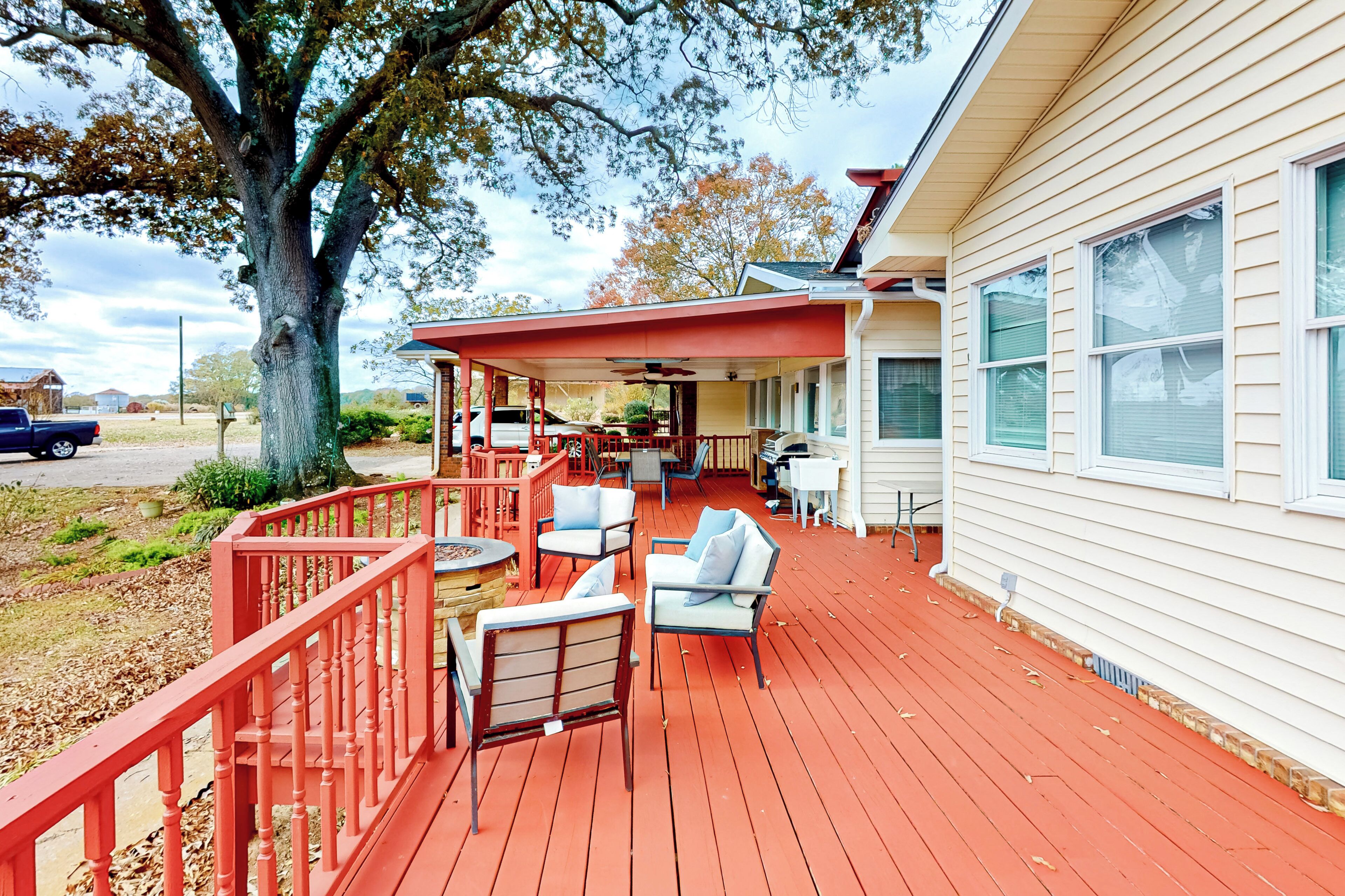 A covered deck with outdoor furniture, a large tree, and a house with white siding.