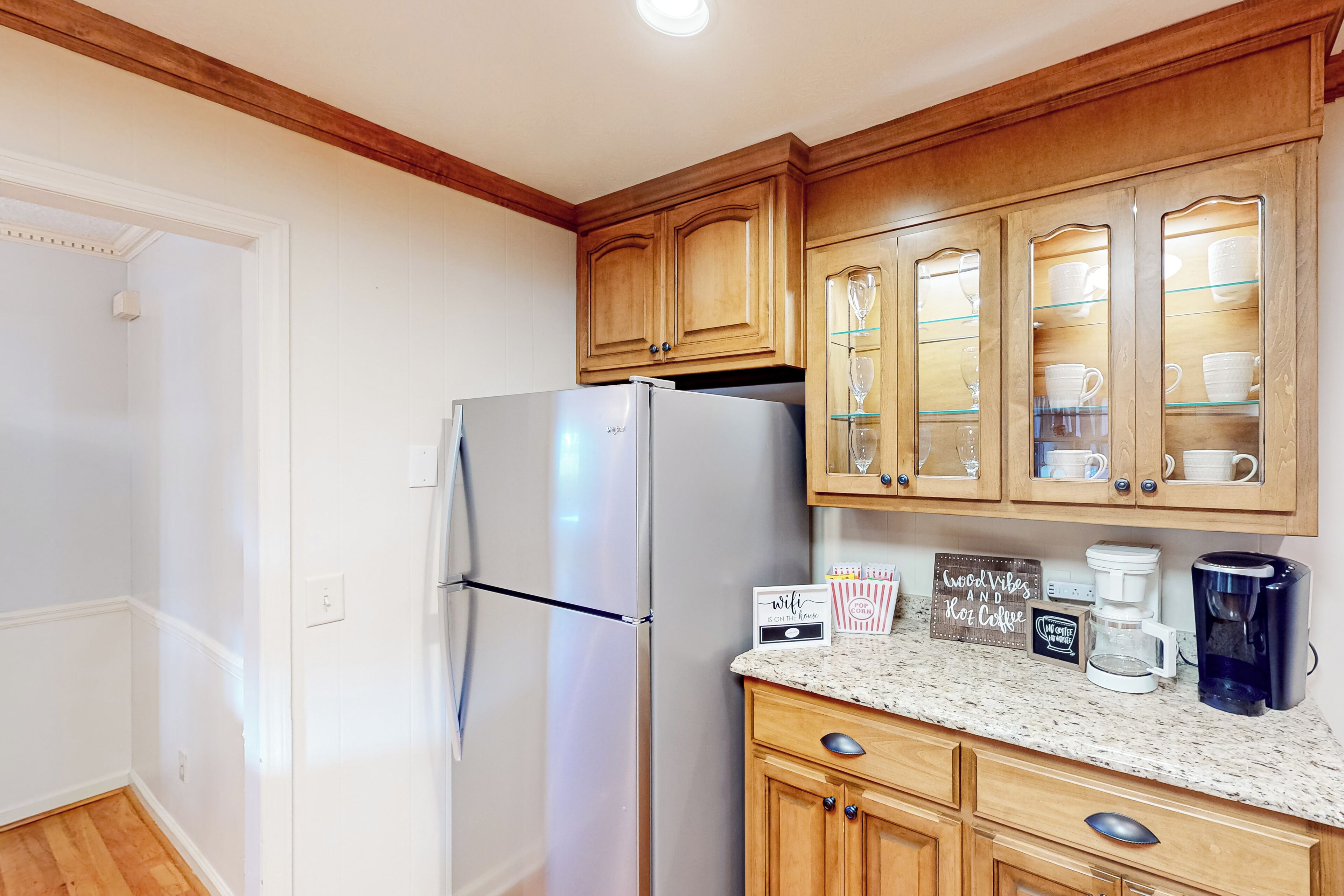 A kitchen with wooden cabinets, a stainless steel refrigerator, a granite countertop, and a coffee maker.