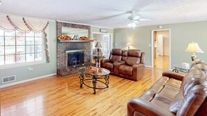 A spacious living room with a fireplace, leather sofas, and a wooden floor. - 4BR Waterview Home w/ Pool, Fire Pit & Fishing (Griffin)