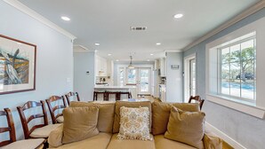 A spacious living room with a beige sectional sofa, wooden chairs, and a large window providing a view of the outdoors. - Dairy Cottage w/ Scenic Views, Outdoor Grilling (Tylertown)