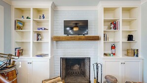 A living room with a fireplace, white brick walls, and built-in shelving with books and decorative items. - Dairy Cottage w/ Scenic Views, Outdoor Grilling (Tylertown)