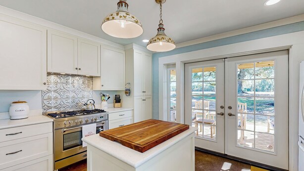 A kitchen with white cabinets, a stove, and a wooden island. There are two pendant lights and a view of the outdoors through a glass door. - Dairy Cottage w/ Scenic Views, Outdoor Grilling (Tylertown)