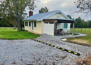 Une petite maison de plain-pied avec un garage, une véranda couverte avec des chaises et une allée gravillonnée.