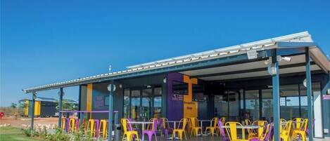 A modern building with a covered outdoor seating area featuring colorful chairs and a reception desk.