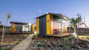 A modern building with a number '9' on its side, a covered outdoor seating area with chairs, and a pathway leading to the entrance. - SleepOver Colesberg (Colesberg)